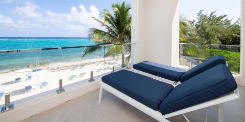 This image shows a tranquil beachfront balcony with a scenic view of a turquoise sea and a sandy beach