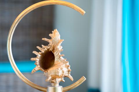 The image shows a decorative object featuring a metallic spiral stand with a gold-colored conch shell affixed to it