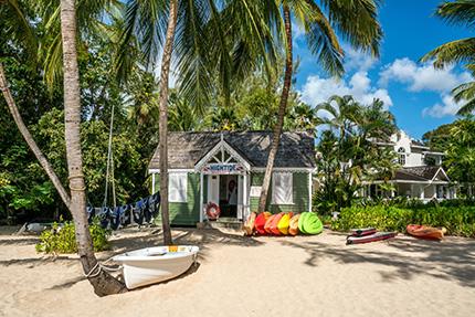 The image shows a picturesque beach setting with a small, charming surf shop nestled among palm trees