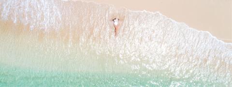 This image shows an aerial view of a beach with a sandy shoreline being washed by clear, turquoise waters