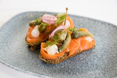 The image displays an appetizing serving of smoked salmon on a slice of dark rye bread, garnished with various toppings