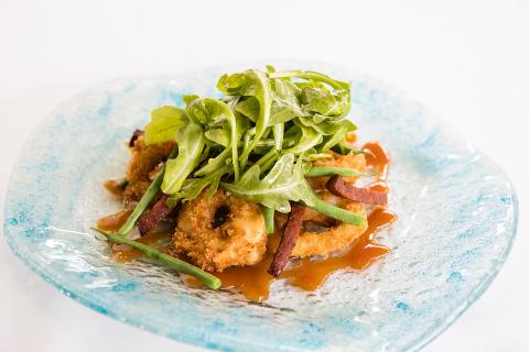 The image shows a beautifully plated dish consisting of breaded and fried seafood, possibly shrimp, garnished with fresh green mâche (also known as lamb