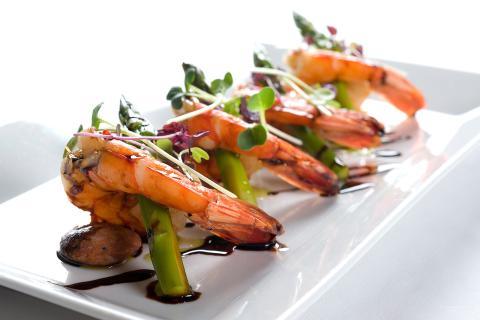 This image features a gourmet dish consisting of large, cooked prawns elegantly arranged on a rectangular white plate