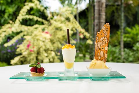 This image displays a beautifully presented trio of desserts, set against a lush garden backdrop