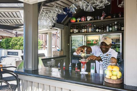 This image captures a cheerful bartender in the process of preparing a cocktail at an outdoor bar setting