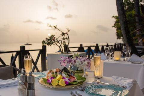 This image depicts a beautifully arranged dining setting by the seaside during sunset