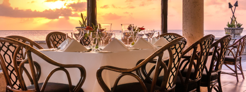 This image features a beautifully set dinner table in an outdoor eating area with a view of the sea