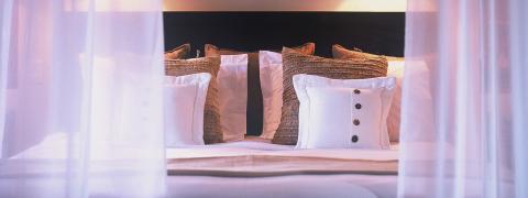 The image shows a neatly arranged bed with several pillows, each with different designs and textures