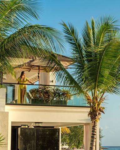 This image shows a woman standing on the balcony of a modern beachfront house