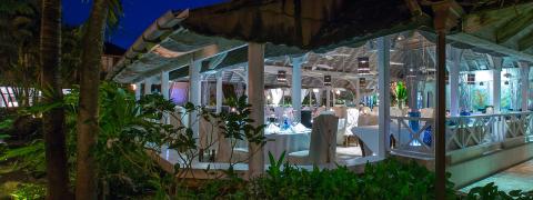 The image shows a tropical-themed outdoor dining area during the evening
