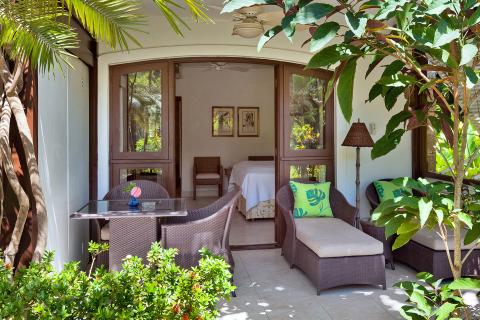 This image shows a cozy and inviting outdoor sitting area right next to what appears to be a bedroom, located within a lush garden setting