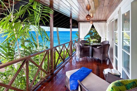 This image features a cozy, tropical balcony setting overlooking a stunning beachfront