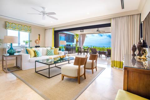 This image features a luxurious and spacious living room that seamlessly opens to an outdoor patio with a breathtaking ocean view
