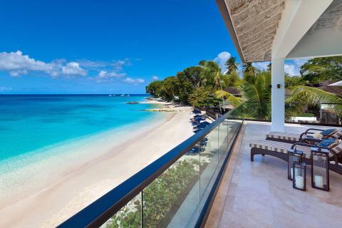This image showcases a breathtaking view from a balcony looking out over a vibrant blue ocean and a scenic beach