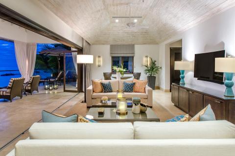This image shows a luxurious, modern living room with an open view to a scenic outdoor terrace overlooking the ocean