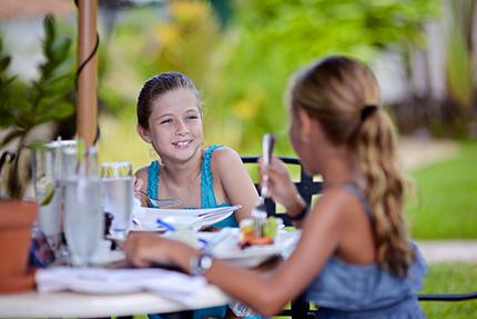 In the image, two young girls are sitting at an outdoor dining table, likely enjoying a meal together