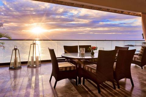 This image depicts a beautifully set outdoor dining area, likely on a patio or terrace, with a stunning ocean view