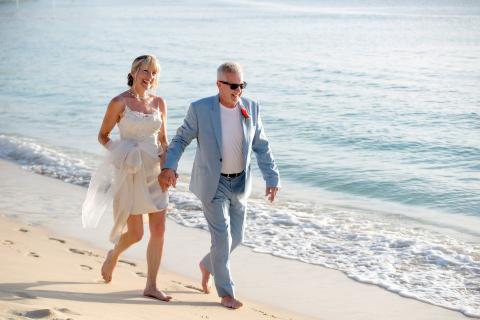 This image captures a joyful moment of a bride and groom walking hand in hand along a sandy beach