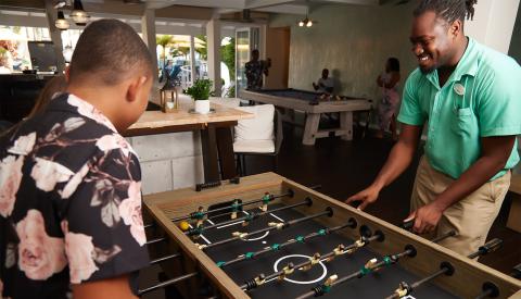 This image shows two people playing foosball in an indoor setting that resembles a bar or a recreational area of a hotel