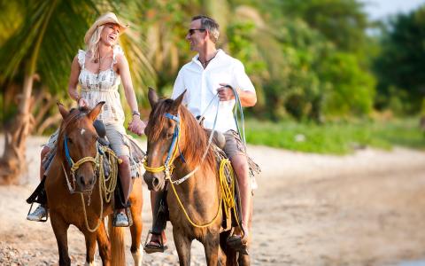 The image features a happy couple riding horses on a sandy beach