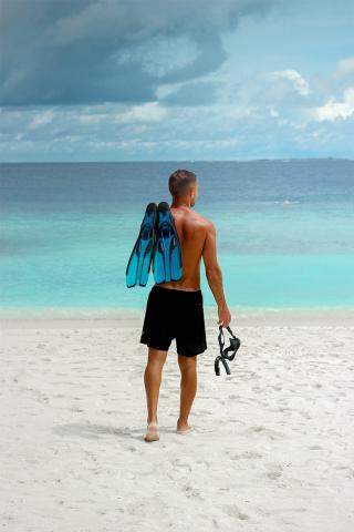This image shows a man standing on a sandy beach, looking out towards a tropical sea