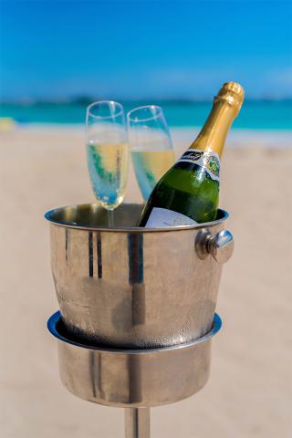 This image features a tranquil beach setting with a bottle of champagne in an ice bucket and two filled champagne glasses on a table