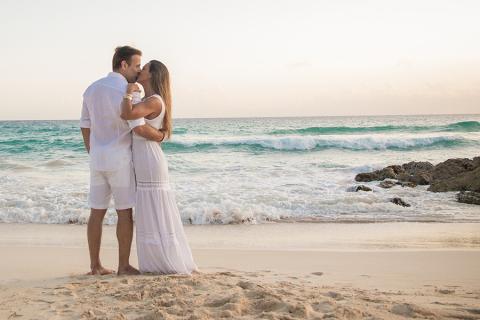 The image depicts a couple standing on a beach at sunrise or sunset