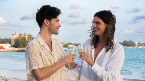 The image shows two men enjoying a moment together at a beachfront setting