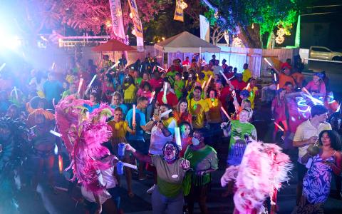 This image captures a vibrant nighttime street festival or parade, with a crowd of people celebrating energetically