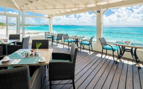This image shows a seaside dining area with a beautiful view of a pristine beach and turquoise ocean