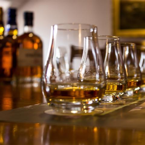 The image shows a row of whisky glasses, each partially filled with amber-colored whisky