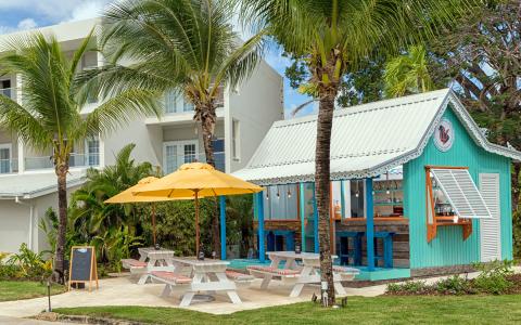 This image shows a vibrant tropical setting with a small, charming turquoise bar building featuring a white roof and decorative trim