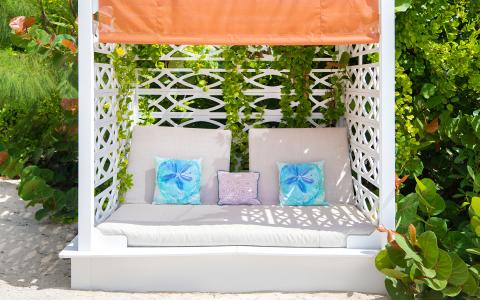 This image features a charming garden lounge bed located under a white latticed canopy with an orange top