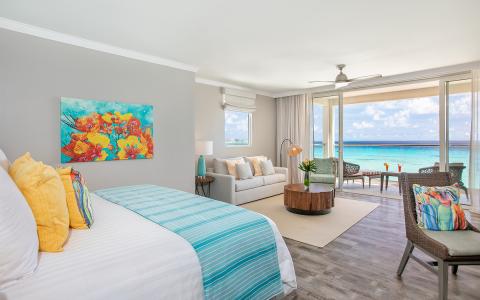 This image depicts a well-furnished hotel room that offers a panoramic view of the ocean