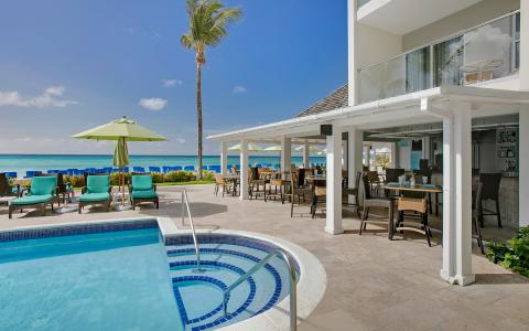 This image shows a luxurious outdoor setting that includes a swimming pool and a dining area at a beachfront location