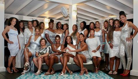 This image features a group of women dressed in elegant, silver and grey toned outfits, posing together at what appears to be a formal event