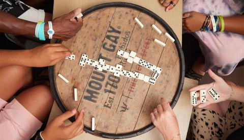 This image shows a group of people engaging in a game of dominoes on a wooden barrel-style table