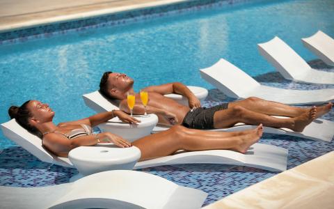 This image depicts a man and a woman relaxing on sun loungers in a swimming pool