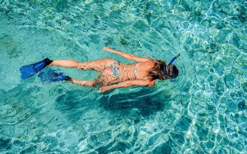 The image shows a person snorkeling in a clear, turquoise body of water