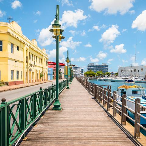 This is an image of a scenic waterfront boardwalk lined with colorful buildings on one side and a marina with various boats on the other