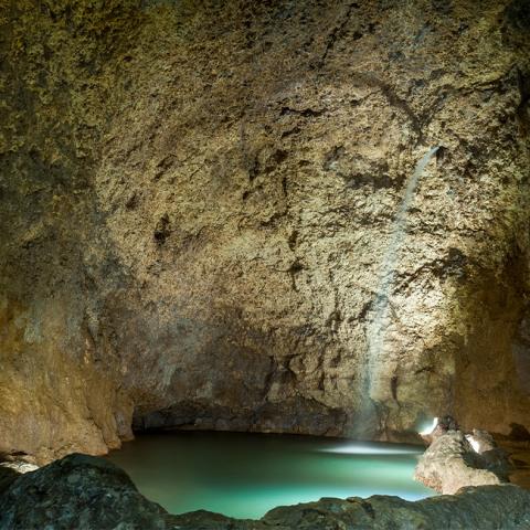 The image shows the interior of a large cave with a subterranean water body
