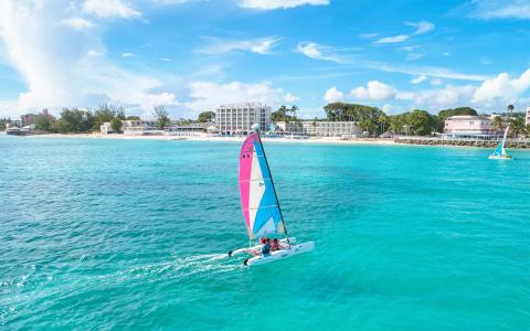 The image shows a breathtaking aerial view of a beach with a small sailboat navigating the clear turquoise waters