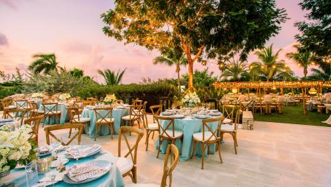 The image depicts an elegantly arranged outdoor event, possibly a wedding reception, set during sunset