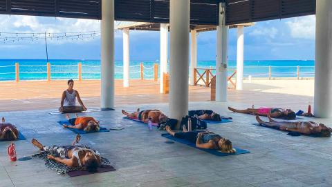 This image depicts a yoga class taking place in a beautiful, open-air structure overlooking the beach