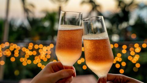 The image shows two hands clinking two champagne glasses, likely in a celebratory toast