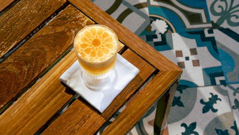 This image shows a glass of a frothy beverage, likely a cocktail or a speciality drink, topped with an interesting decorative slice of citrus, possibly an orange, which resembles a mandala-like pattern