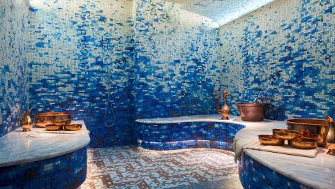 The image shows a beautifully designed bathroom, richly adorned with blue mosaic tiles covering the walls and ceiling, giving the space a vibrant and luxurious feel
