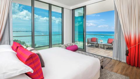 The image shows a modern hotel room with a stunning ocean view