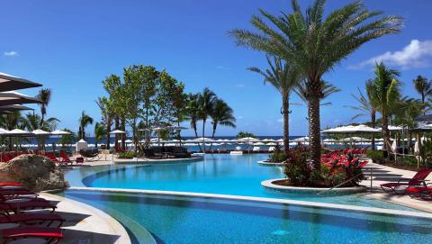 The image depicts a luxurious, tropical resort setting with a large, inviting swimming pool