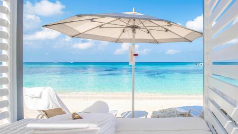 This image shows a luxurious beachside setting, viewed from a shaded area under a white umbrella
